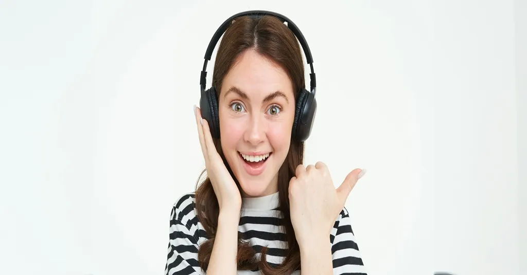 Happy young woman pointing sideways while wearing [Brand] over-ear wireless headphones