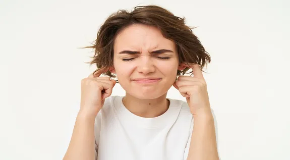 Woman covering her ears from loud noise and feeling uncomfortable