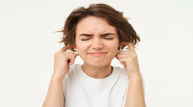 Woman covering her ears from loud noise and feeling uncomfortable