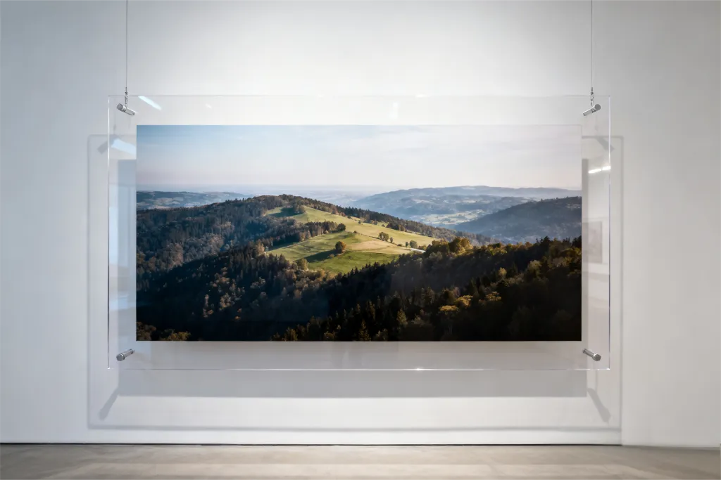 A minimalist, unframed photo display. A large landscape photograph is suspended between two clear acrylic sheets, held by nearly invisible corner mounts on a white wall. 