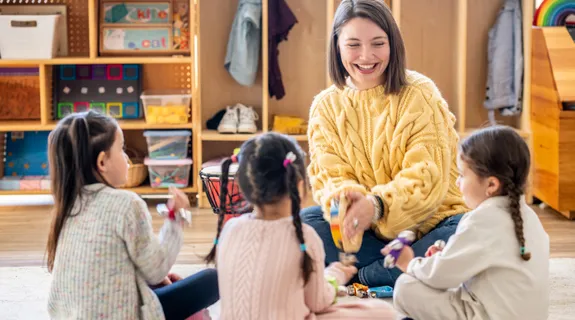 一人の女性教師が3人の子どもたちと接し、異年齢保育の年間指導計画を理解し、作成しようとしています。