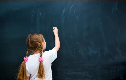小さな女の子が大きいサイズの黒板に字を書いています。
