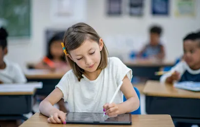 学校向けプロジェクターがある教室で小さな女の子がタブレットでノートを取っている