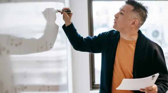 男性がガラスボードに文字や図を描いている