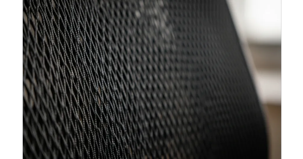 Macro photography of black high-tension mesh on an ergonomic desk chair, highlighting the breathable weave pattern for thermal regulation and airflow.