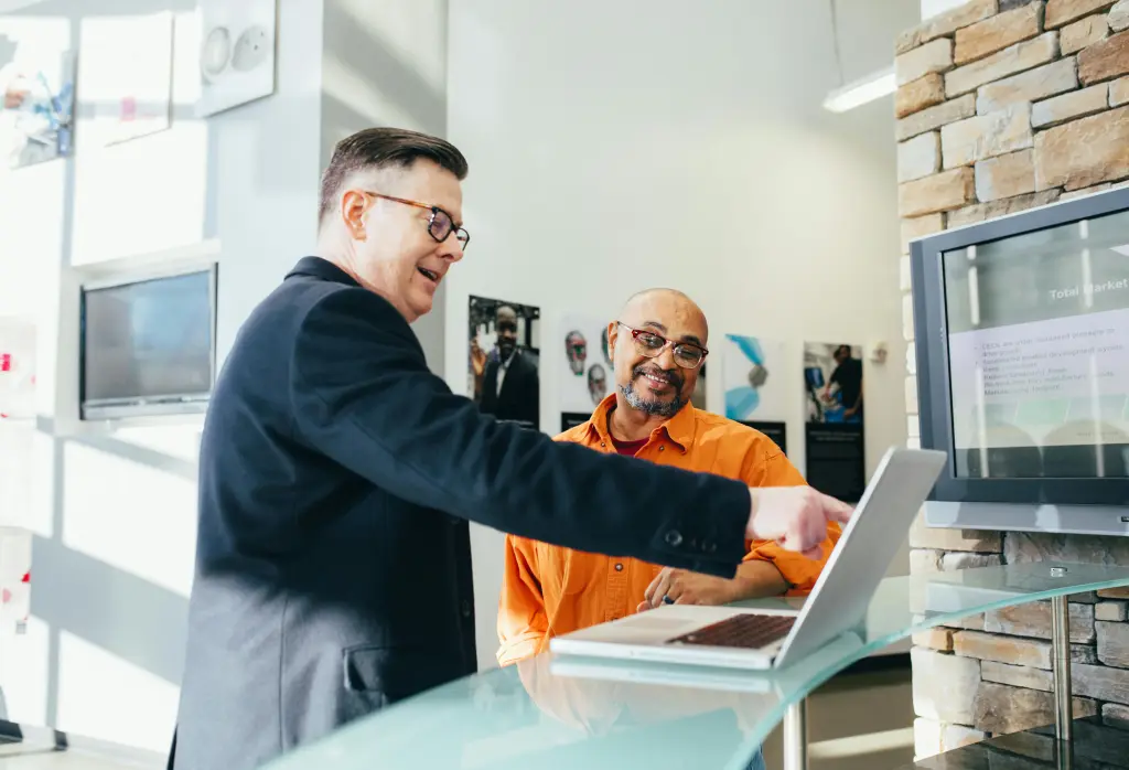 Two businessmen smiling and shaking hands to finalize a deal in front of a 30-inch touch screen monitor displaying the signed agreement