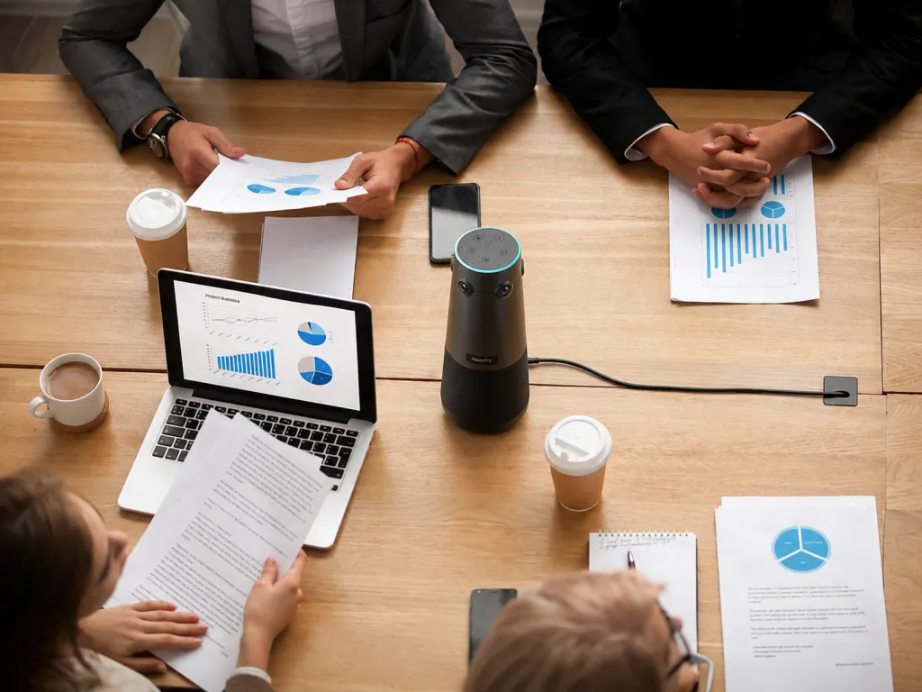 360Alien conference camera placed at the center of a business consultation meeting table, connected to power and surrounded by professionals reviewing reports, charts, and presentation materials.