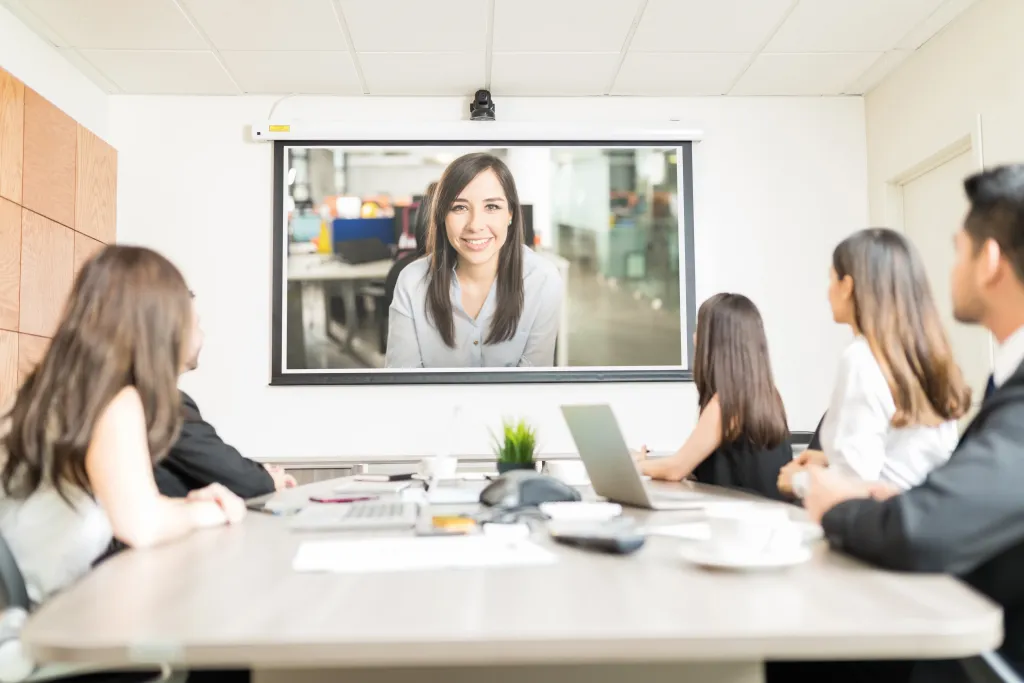Professionelles Team in einem modern ausgestatteten Konferenzraum während einer hybriden Videokonferenz mit Remote-Teilnehmern auf einem großen Display