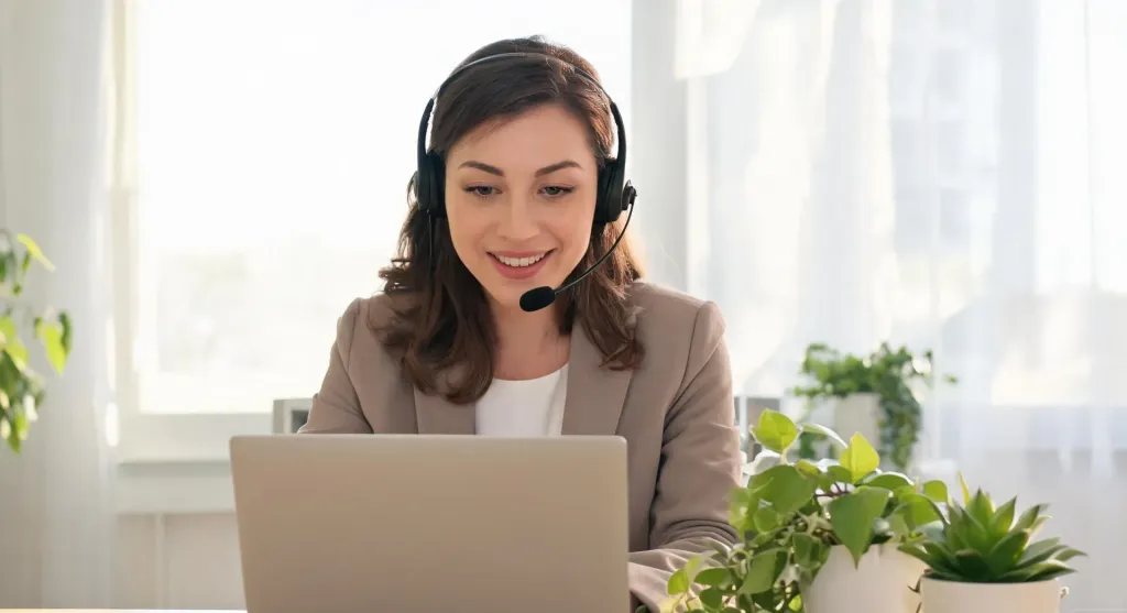 Online English teacher wearing a professional wireless headset while conducting a virtual lesson on a laptop in a bright modern home office