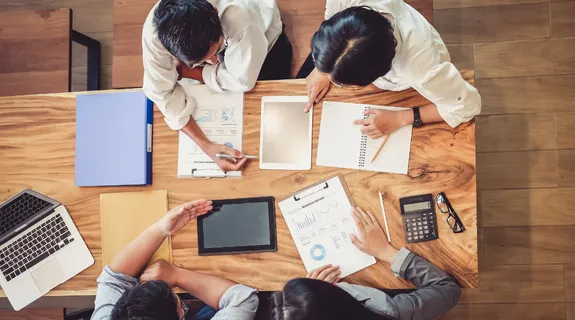 オフィスで4人の社員が「ダメな会社ほど会議が多い」について話し合っている。