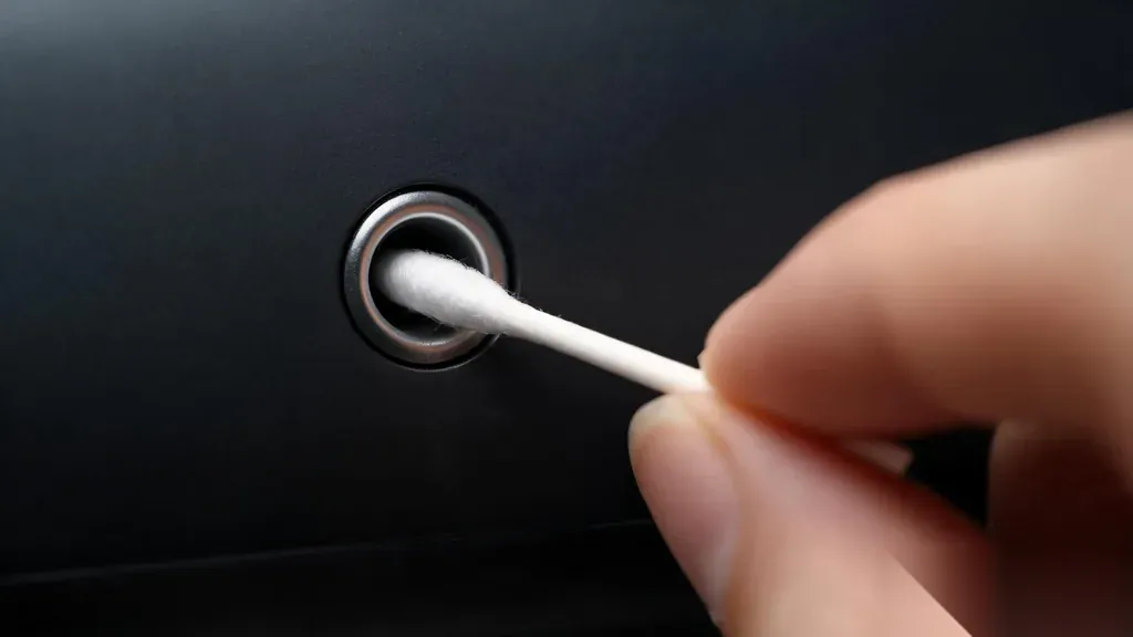 Macro close-up of a cotton swab being inserted into a metal headphone audio jack port for cleaning