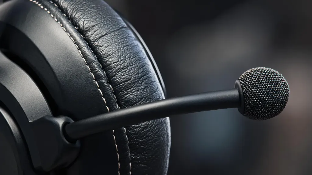 Close-up detail of a black over-ear headset showing memory foam ear cushions, protein leather stitching, and boom microphone arm