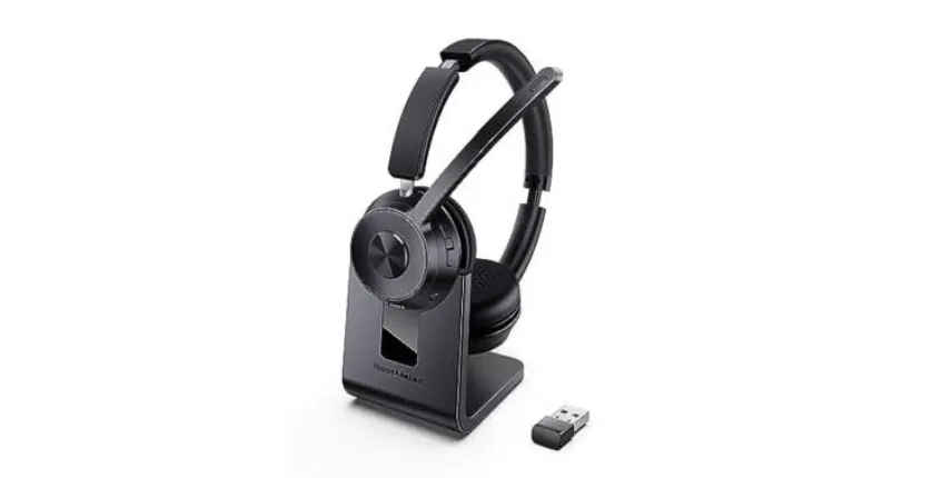 A wireless communication headset resting on a matching desktop charging stand, with a USB wireless dongle placed beside it.