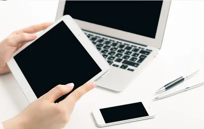 一人がデジタルメモを手に持ち、机の上にパソコンとスマホがある