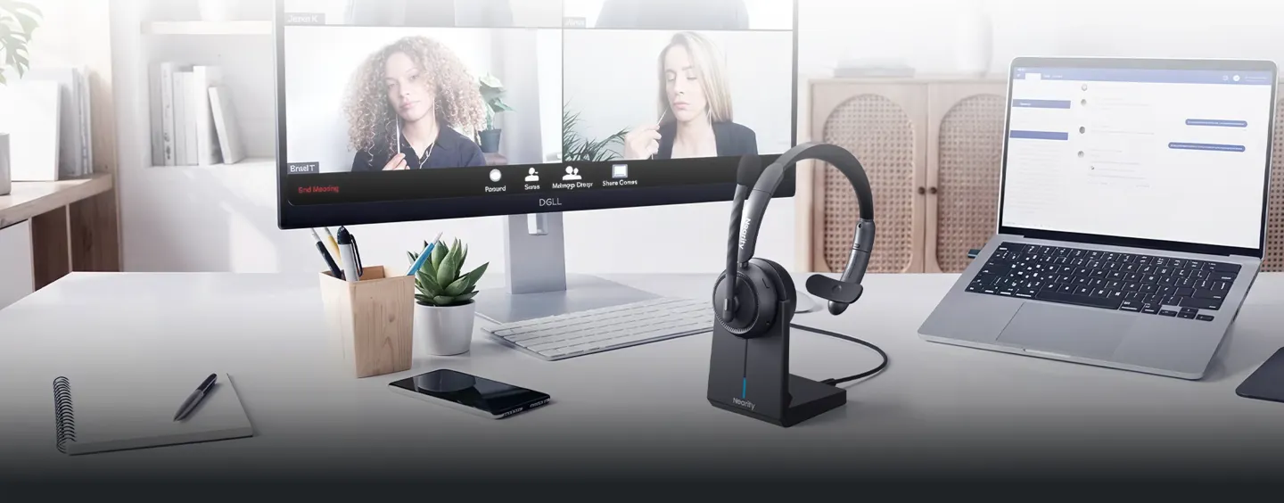 A premium single ear wireless headset with mic for pc resting on its charging dock on a modern corporate office desk setup with a laptop.