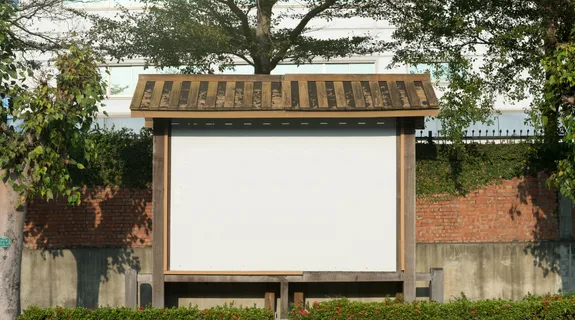 庭に大きな木製掲示板があり、陽の光に照らされて静けさが感じられます。