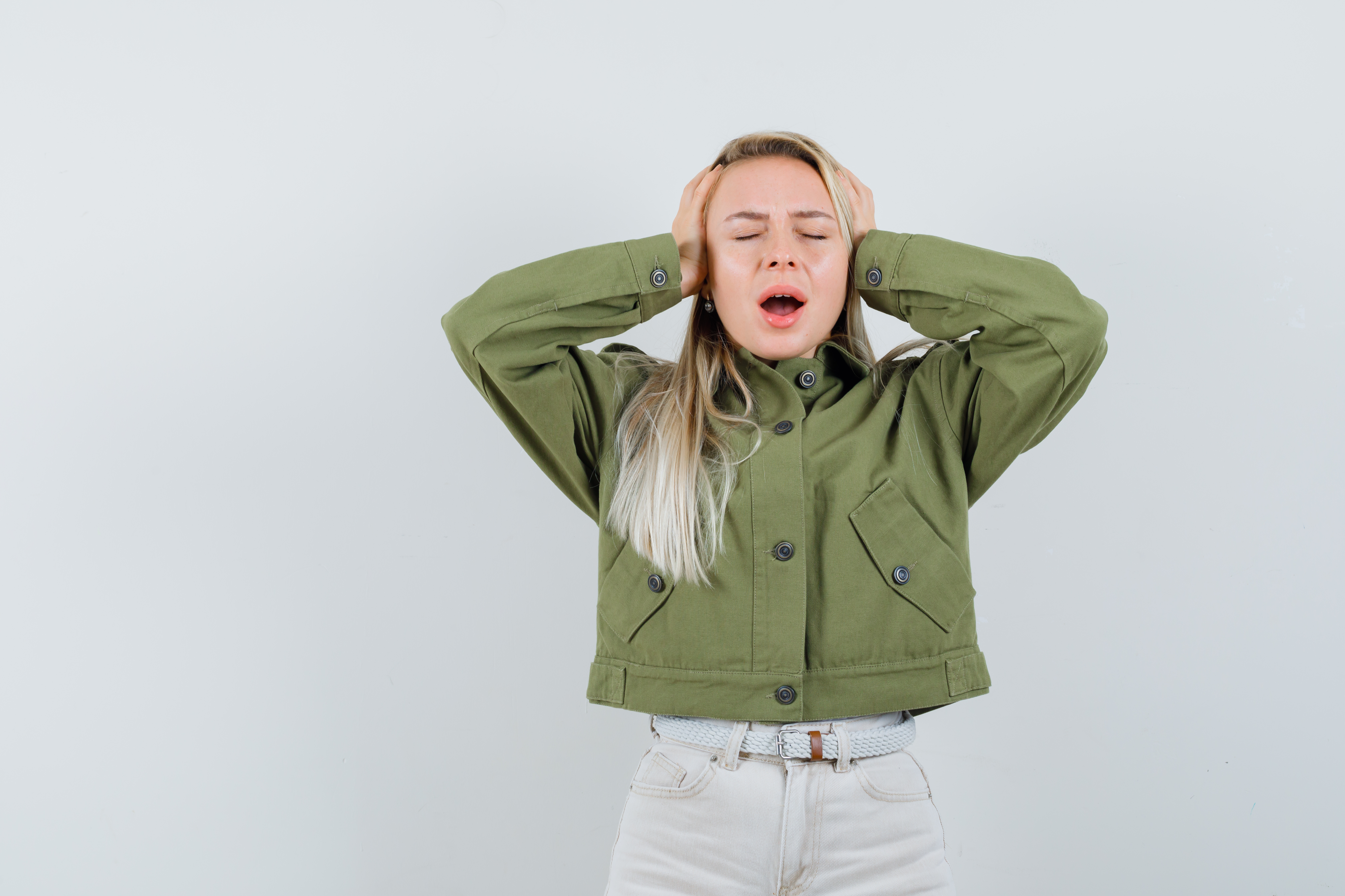 young-female-clasping-head-with-hands-green-jacket-looking-bored-front-view.jpg