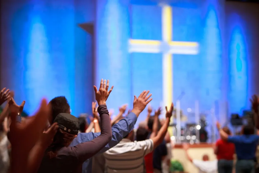 Congregants raising hands in worship before a glowing cross in a modern church sanctuary