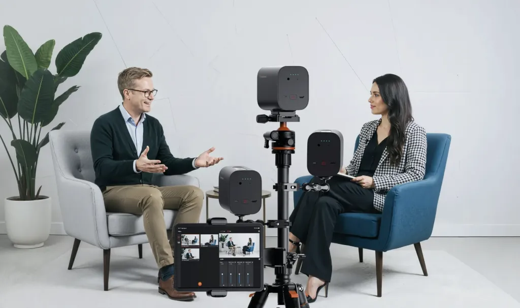 Professional multi-camera interview setup with three compact streaming cameras on tripods capturing a two-person conversation in a modern studio