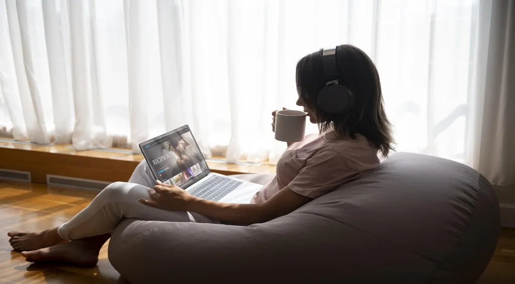 Woman wearing wireless headphones while relaxing and using a laptop at home
