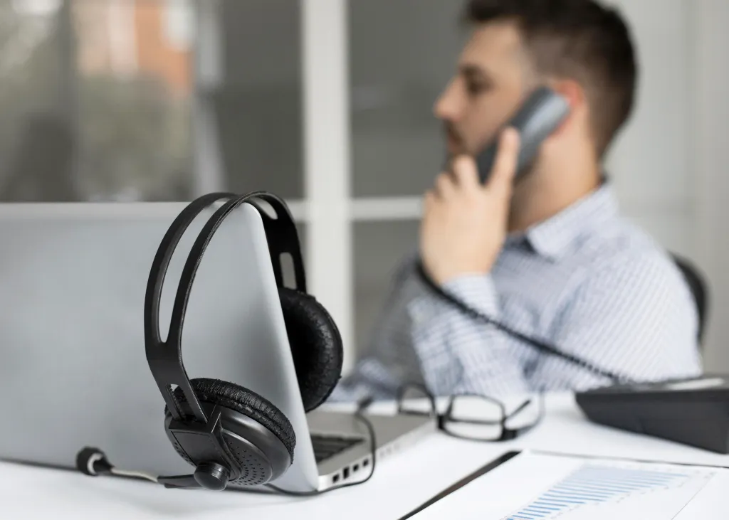 Close-up of a man taking a phone call with his headset resting on one side, working at his desk in an office setting.