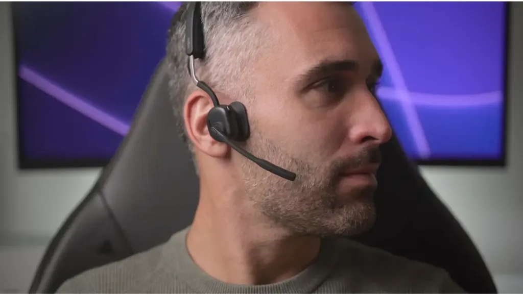 Andy wearing Shokz Open Meet open-ear headset, showing the premium dual-pitch bone and air conduction design, with busy indicator LED active during a video call.