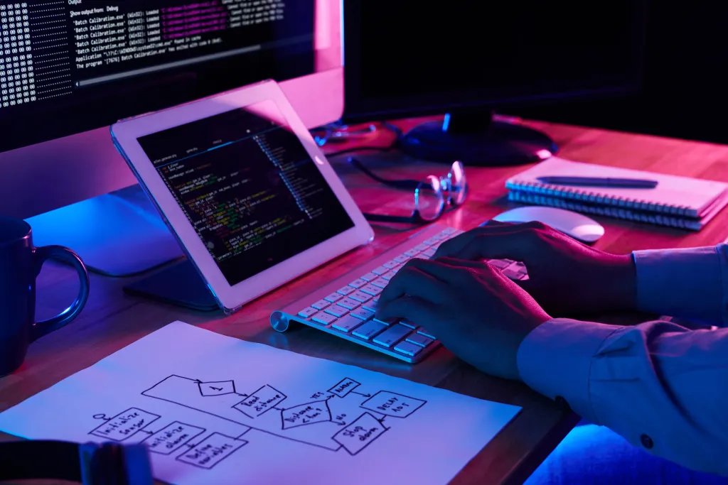 A close-up view of a programmer typing code on a compact keyboard at a neon-lit desk setup, showing why developers look for the best noise cancelling headphones for coding.