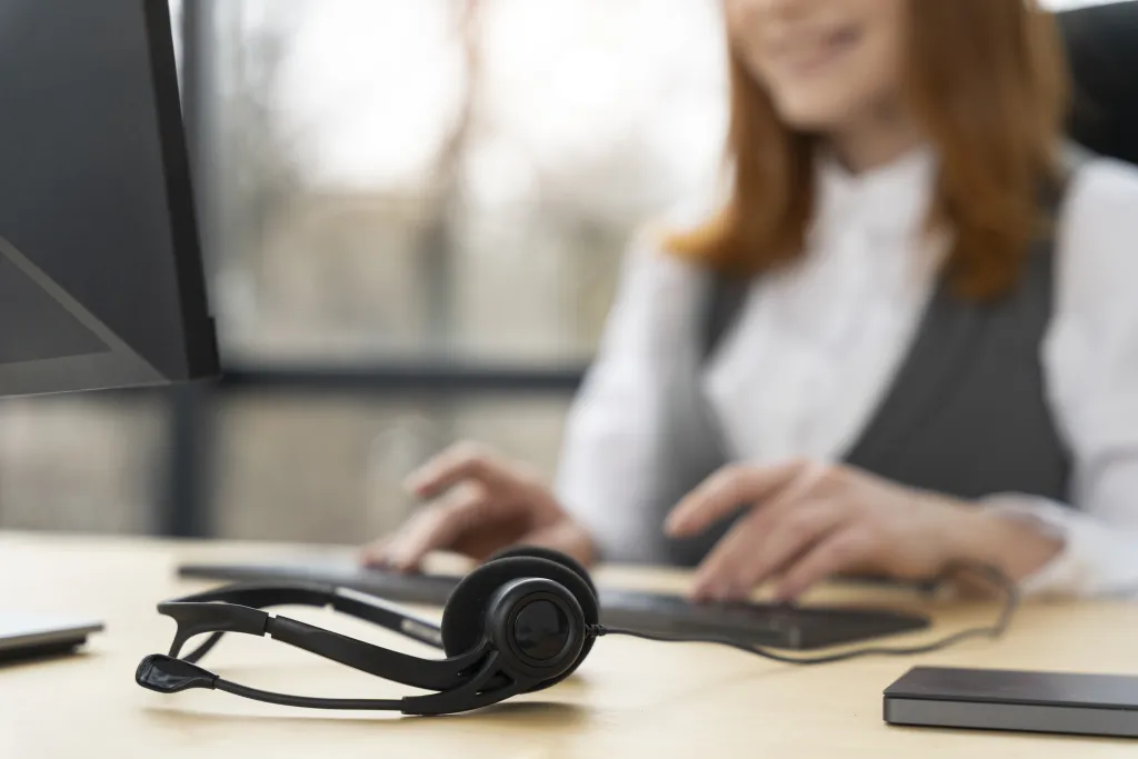A professional wireless usb headset for call cente resting on an office desk while a staff member works in the blurred background.