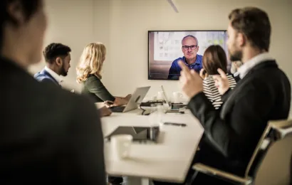 Professionelles Hybrid-Meeting im modernen Konferenzraum mit zentraler 360-Grad-Kamera und Teilnehmern vor Ort sowie Remote-Kollegen auf einem großen Display