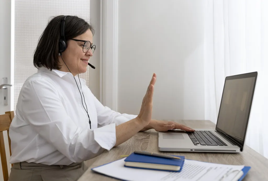 A female teacher wearing a headset to call phone from pc while conducting an online lesson with her students.