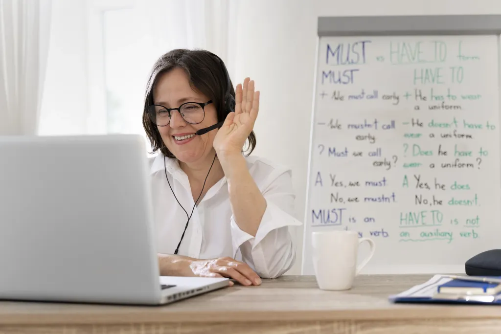 A smiling language teacher waving to her virtual classroom while wearing the wireless headphone for online teaching.