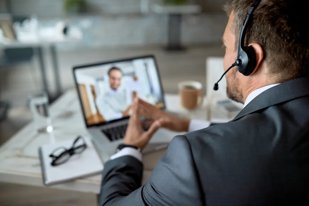 Close-up of an entrepreneur wearing a business wireless headset with a mic while having a virtual business meeting on a laptop.