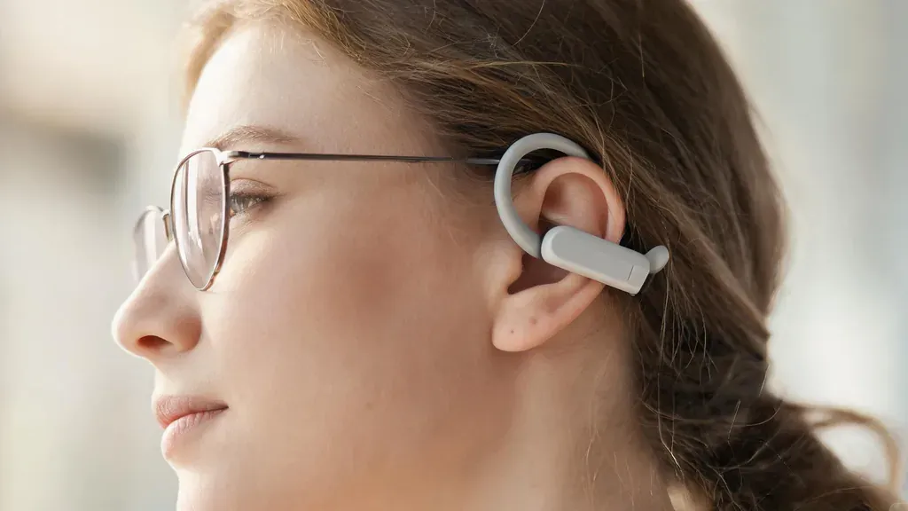 Close-up profile of a woman wearing eyeglasses and open-ear headphones that hook over the ear without pressing the temples