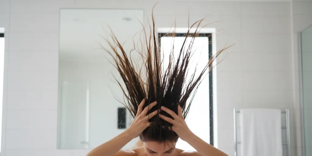 Person flipping head upside down and running damp hands through hair to fluff out a headphone dent and restore natural volume