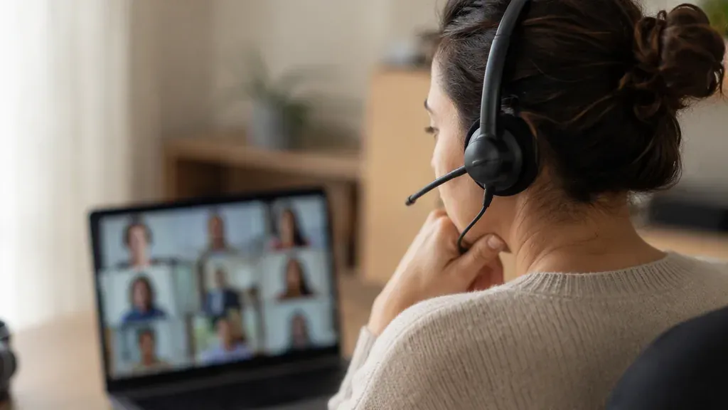 A woman wearing a wireless headset during a video meeting at her home office desk
