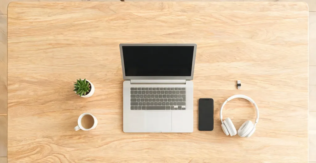 Top-down view of a clean desk with laptop, smartphone, wireless headset, and USB dongle arranged neatly