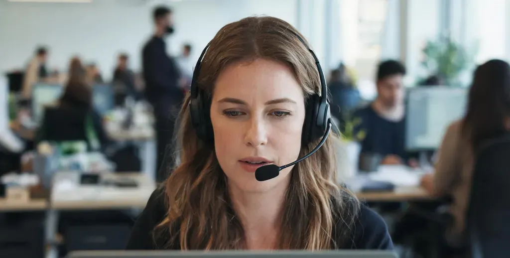 Woman on a call in a busy open office, wearing a noise-cancelling headset with mic