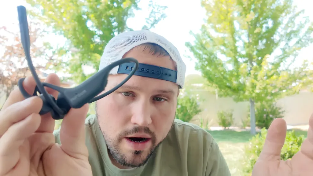 Man holding up a black Nuroum open-ear headset with a boom microphone for demonstration outdoors.