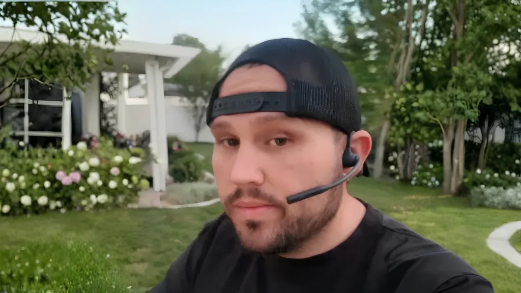 Man wearing a black Nuroum open-ear headset with an extended boom microphone in a backyard setting.