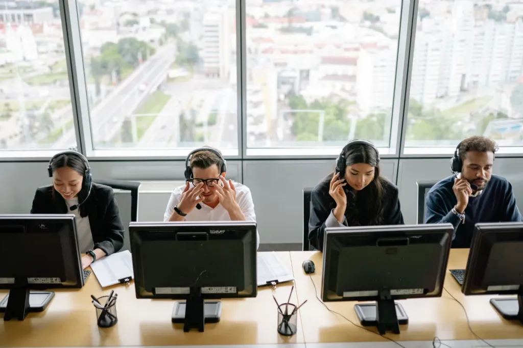 Diverse customer service team wearing phone headsets and operating computers in a modern office environment.