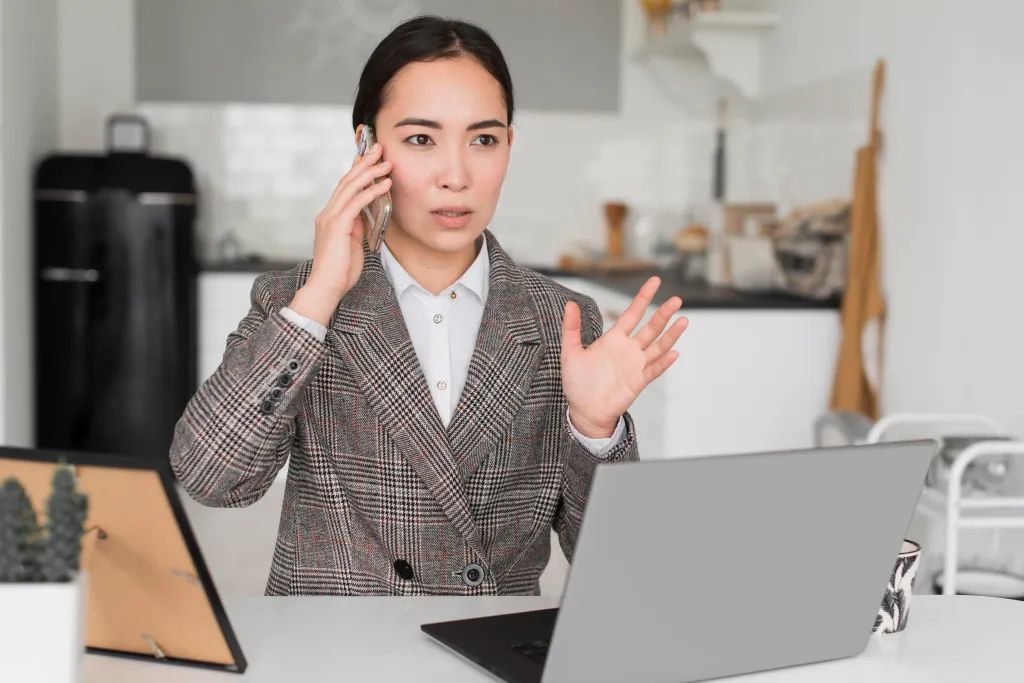 A woman making a phone call on her smartphone while working at her desk in a real estate call center.