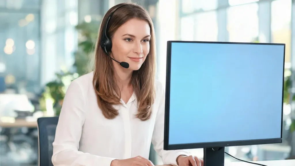 Travel agent smiling while speaking with a customer on a headset, photographed in a bright modern office with warm natural light and soft background blur