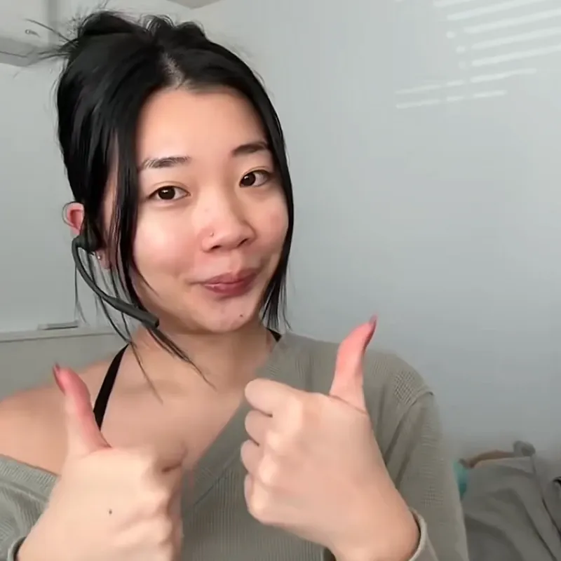 A woman giving two thumbs up while wearing a black Nuroum open-ear headset with a boom mic, showing customer satisfaction.