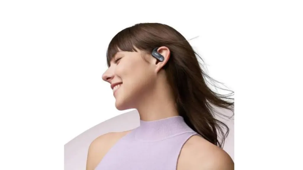 Smiling woman wearing black Shokz open-ear true wireless ear hook earbuds.