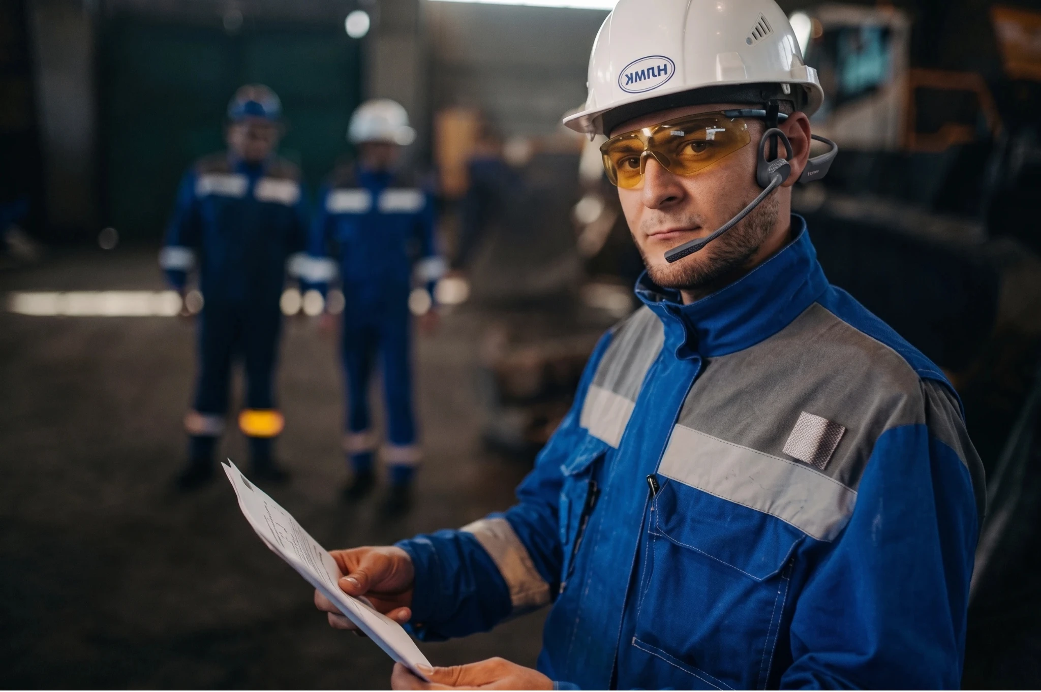 QA inspector with hard hat and open ear headset reviewing tablet