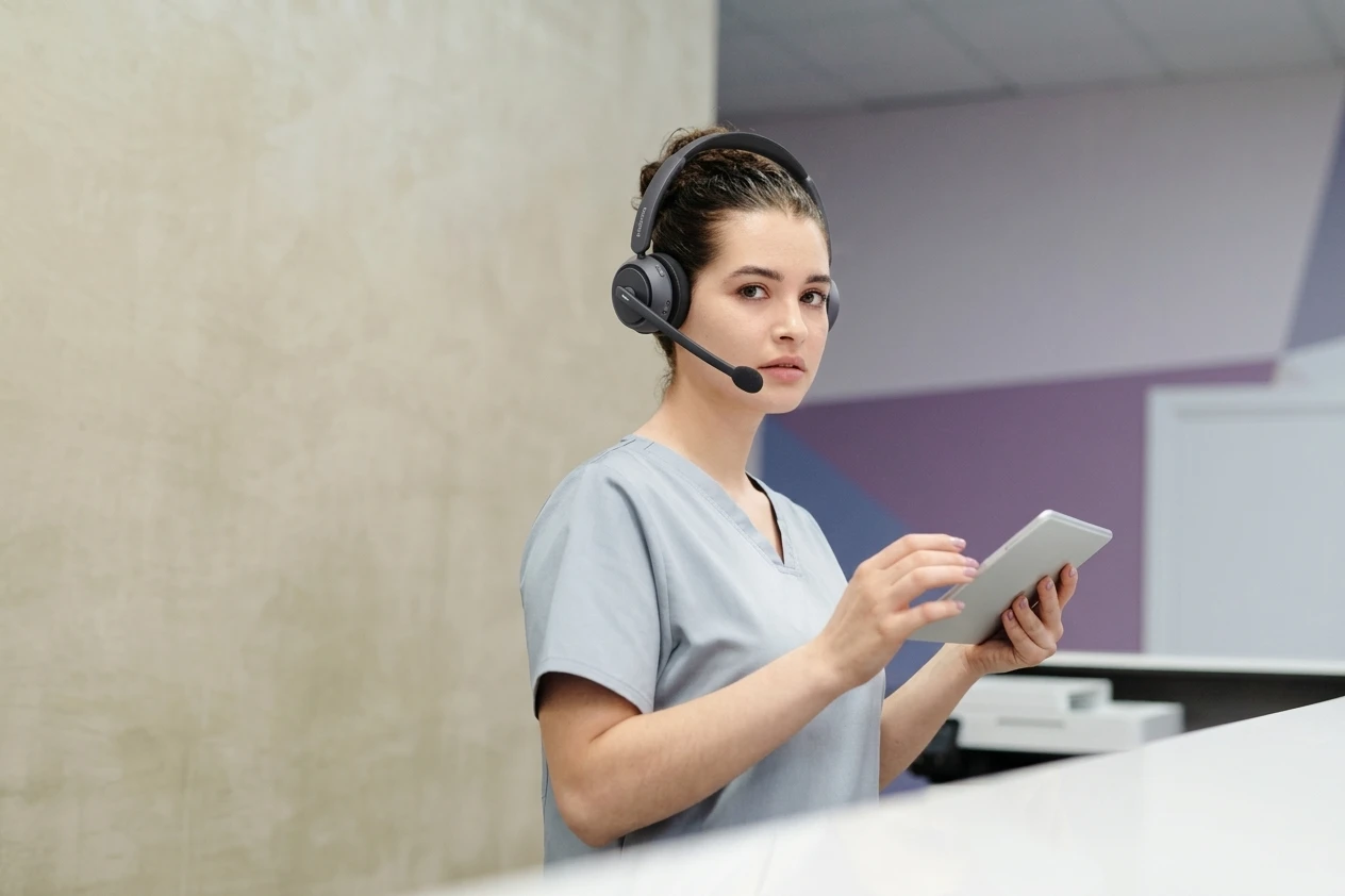 Hospital receptionist in scrubs helping a patient while wearing single-ear headset