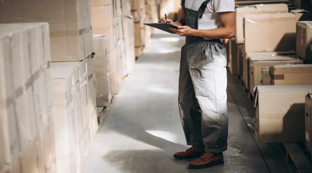 A warehouse worker checking inventory in a storage facility, demonstrating the need for stable trucking headsets during high-velocity logistics operations.